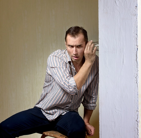79331574-man-with-a-glass-listening-to-a-conversation-through-the-wall.webp
